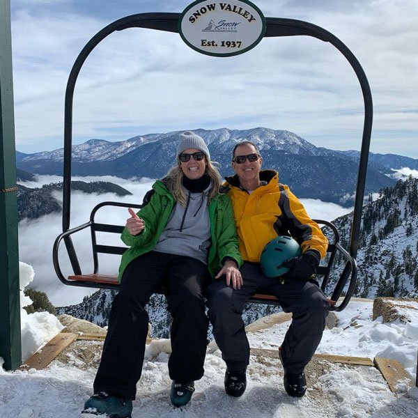Two adults in ski gear sitting on a detached Snow Valley chairlift with a great background view